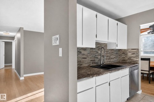 White upper and lower cabinetry, mosaic tile backsplash, black double basin sink with a high arc faucet, and stainless steel dishwasher - #204 7407 171 St Nw, Edmonton, AB 