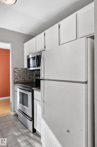 White upper and lower cabinetry, stainless steel oven, built-in microwave, tiled backsplash, and tiled flooring - #204 7407 171 St Nw, Edmonton, AB 