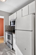 White upper and lower cabinetry, stainless steel oven, built-in microwave, tiled backsplash, and tiled flooring - 