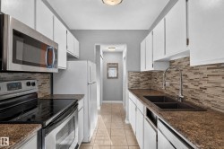 Galley kitchen featuring white cabinetry, stainless steel appliances, a mosaic tile backsplash, and a double basin sink with an extendable faucet - 