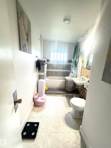 Bathroom featuring a white bathtub, ceramic wall tiling, a pedestal sink, and a toilet - 5019 48 Avenue, Onoway, AB - Indoor