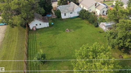 Expansive green lawn with mature trees and perimeter fencing. showing the home and garage - 5019 48 Avenue, Onoway, AB - Outdoor