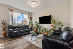 Living area featuring wood-finish flooring, a large window with wrought iron detailing, and a modern crystal chandelier - 