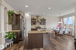 Open-concept kitchen featuring wood-finish flooring, dark wood cabinetry, and granite countertops - 
