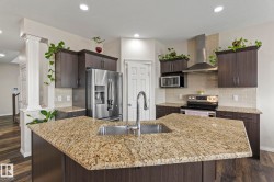 Kitchen featuring a spacious island with an undermount sink and polished chrome faucet, granite countertops, dark wood-finish cabinetry, stainless steel appliances, and a tiled backsplash - 