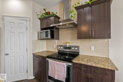 Kitchen featuring dark wood-finish cabinetry, light-toned subway tile backsplash, speckled countertops, stainless steel appliances, and a white paneled door - 