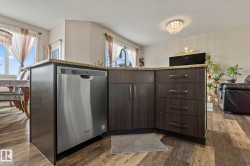 Kitchen island featuring a stainless steel dishwasher, dark wood-finish cabinetry, sleek hardware, and a granite countertop - 