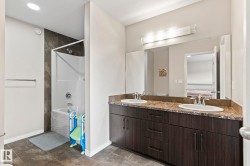 Bathroom featuring a dual-sink vanity with a speckled countertop, dark wood-finish cabinetry, and a full-width mirror - 