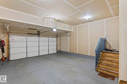 Spacious garage featuring a durable epoxy-coated concrete floor, white panel garage door, built-in overhead lighting, and interior access via wooden stairs with blue railing - 