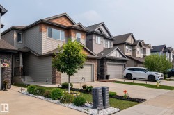 Modern residential exterior featuring gray siding, brown shake accents, stone veneer detailing, a two-car garage, and landscaped front yard with concrete driveway - 