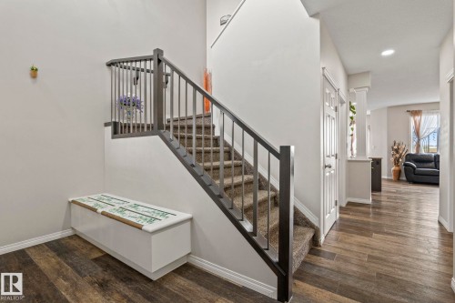 Grand entryway featuring wood-finish flooring, a carpeted staircase with dark wood newel posts and railings, white baseboards, and a white interior door with paneling - 2131 51 Sw, Edmonton, AB - Indoor Photo Showing Other Room