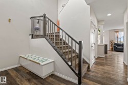 Grand entryway featuring wood-finish flooring, a carpeted staircase with dark wood newel posts and railings, white baseboards, and a white interior door with paneling - 