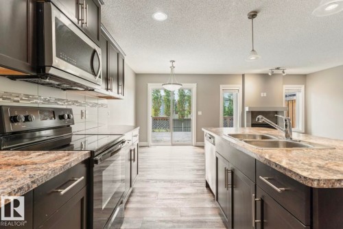 Modern kitchen featuring dark cabinetry, stainless steel appliances, and wood-finish flooring - 79 Catalina Crest, Fort Saskatchewan, AB - Indoor Photo Showing Kitchen With Double Sink With Upgraded Kitchen