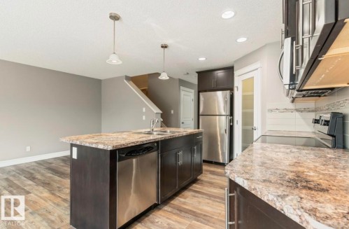 Contemporary kitchen featuring an island with a double basin sink and integrated dishwasher, stainless steel appliances, dark wood-finish cabinetry, and stone-finish countertops - 79 Catalina Crest, Fort Saskatchewan, AB - Indoor Photo Showing Kitchen With Double Sink With Upgraded Kitchen