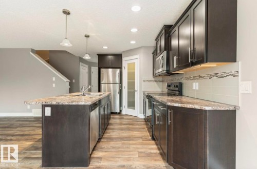 Kitchen featuring dark wood-finish cabinetry, stainless steel appliances, a spacious island with sink, pendant lighting, and wood-finish flooring - 79 Catalina Crest, Fort Saskatchewan, AB - Indoor Photo Showing Kitchen With Upgraded Kitchen