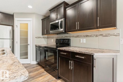 Kitchen featuring dark wood-finish cabinetry with brushed nickel hardware, laminate countertops, and a subway tile backsplash with decorative accents - 79 Catalina Crest, Fort Saskatchewan, AB - Indoor Photo Showing Kitchen