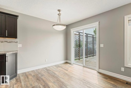 Dining area featuring wood-finish flooring, a modern ceiling light fixture, and a sliding glass door leading to an outdoor deck with lattice railing - 79 Catalina Crest, Fort Saskatchewan, AB - Indoor Photo Showing Other Room