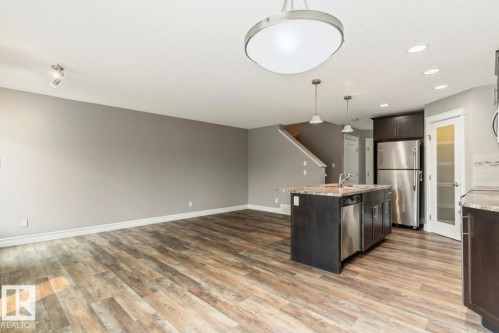 Open-concept living space featuring wood-finish flooring, a kitchen island with a sink and integrated dishwasher, stainless steel appliances, and a pantry with a frosted glass door - 79 Catalina Crest, Fort Saskatchewan, AB - Indoor Photo Showing Kitchen