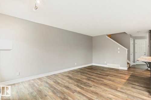 Spacious living area featuring wood-finish flooring, light gray walls, white baseboards, and a contemporary track light fixture - 79 Catalina Crest, Fort Saskatchewan, AB - Indoor Photo Showing Other Room