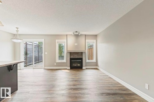 Living area featuring wood-finish flooring, a contemporary fireplace with a stone surround, and light-toned walls - 79 Catalina Crest, Fort Saskatchewan, AB - Indoor Photo Showing Living Room With Fireplace