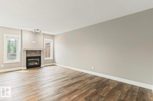 Open-concept living space featuring wood-finish flooring, a contemporary fireplace with a stone-tile surround, and two windows providing natural light - 79 Catalina Crest, Fort Saskatchewan, AB - Indoor Photo Showing Living Room With Fireplace