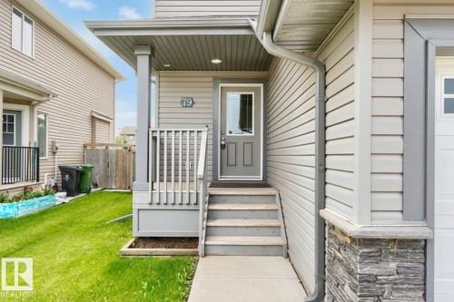 Inviting front entrance featuring a covered porch, wood stairs, a paneled door with glass insert, horizontal siding, and a stone accent column - 79 Catalina Crest, Fort Saskatchewan, AB - Outdoor With Deck Patio Veranda