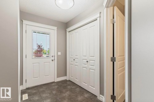 Entryway featuring a white paneled door with glass insert, dark grey tile flooring, and a white bi-fold closet - 79 Catalina Crest, Fort Saskatchewan, AB - Indoor Photo Showing Other Room