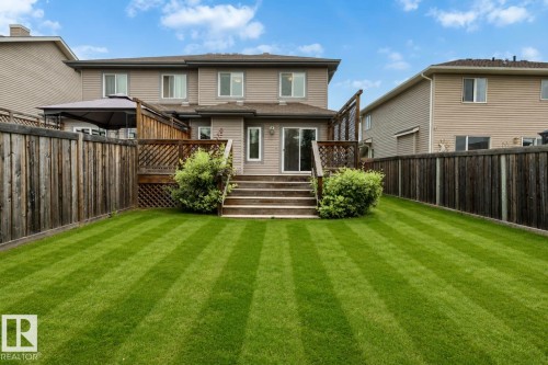 Expansive rear lawn featuring a wooden privacy fence, a multi-level wood deck, and rear home access via sliding glass doors - 79 Catalina Crest, Fort Saskatchewan, AB - Outdoor