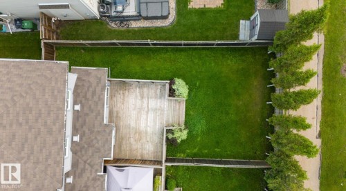 Expansive backyard featuring a multi-level wood-finish deck, lush green lawn, and mature perimeter trees - 79 Catalina Crest, Fort Saskatchewan, AB - 
