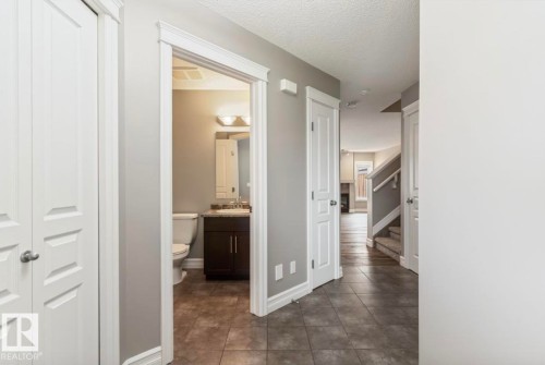 Entryway featuring large format tile flooring, a powder room with a dark wood-finish vanity and granite-style countertop, white trim and baseboards, and a staircase with carpeted treads - 79 Catalina Crest, Fort Saskatchewan, AB - Indoor Photo Showing Other Room