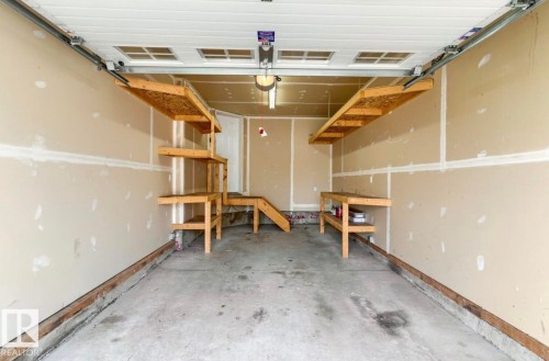 Attached garage featuring a concrete floor, light tan walls, a white overhead door, and built-in wood shelving - 79 Catalina Crest, Fort Saskatchewan, AB - Indoor Photo Showing Garage