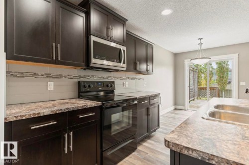 Kitchen featuring dark wood cabinetry, a stainless steel microwave, a black range with an oven, patterned laminate countertops, and a glass tile backsplash - 79 Catalina Crest, Fort Saskatchewan, AB - Indoor Photo Showing Kitchen With Double Sink