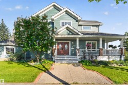 Wood-paneled double entry doors, covered porch with white columns, brick accents on porch pillars, upper-level dormer window, and a concrete pathway with brick edging - 