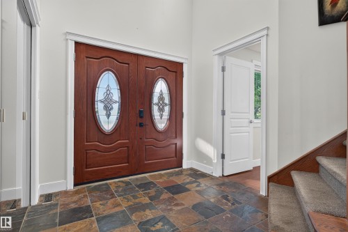Double entry doors with decorative glass inserts, multi-tone slate tile flooring, and a carpeted staircase with wood trim - 1251 Summerside Drive Sw, Edmonton, AB 