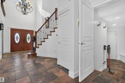 Foyer featuring a grand staircase with wrought iron balusters, double entry doors with decorative glass, and slate tile flooring - 