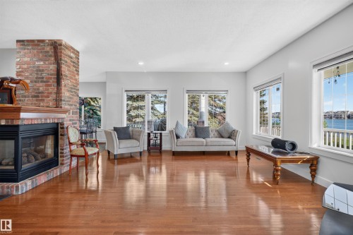 Spacious living area featuring a brick fireplace with a wood mantle, hardwood flooring, recessed lighting, and multiple windows - 1251 Summerside Drive Sw, Edmonton, AB 