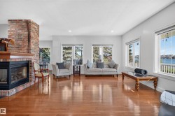 Spacious living area featuring a brick fireplace with a wood mantle, hardwood flooring, recessed lighting, and multiple windows - 