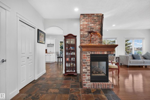 Brick-clad fireplace with wood mantel, tile flooring, wood-finish flooring, white paneled doors, and an arched doorway - 1251 Summerside Drive Sw, Edmonton, AB 