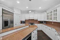 White cabinetry with decorative crown molding, stone countertops, stainless steel refrigerator, built-in range, and dark-toned floor tiles - 