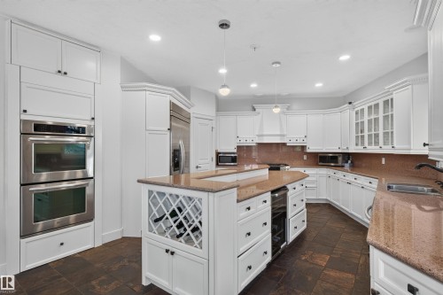 Kitchen featuring white cabinetry, stainless steel double ovens, a center island with built-in wine storage, stone countertops, and dark tile flooring - 1251 Summerside Drive Sw, Edmonton, AB 