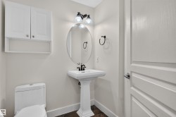 Pedestal sink with black-finish faucet, oval mirror, wall-mounted light fixture, white wall cabinet, and dark-finish flooring - 