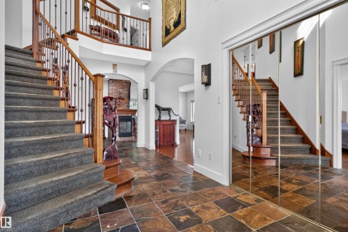 Foyer with natural stone tile flooring, a carpeted staircase with wood banister and wrought iron spindles, and mirrored closet doors - 1251 Summerside Drive Sw, Edmonton, AB 