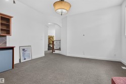 Carpeted interior space with a built-in wood-finish cabinet, arched doorway, and staircase with metal balusters - 