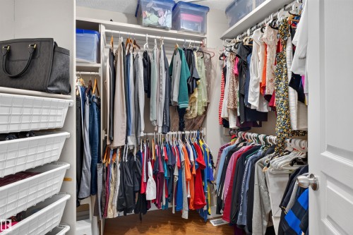 Walk-in closet with multiple hanging rods, built-in shelving, and wood-finish flooring - 1251 Summerside Drive Sw, Edmonton, AB 