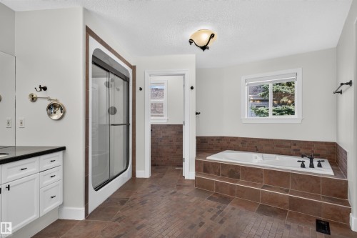 White vanity cabinetry with a black countertop, a framed shower enclosure with sliding glass doors, a built-in bathtub with tiled surround, and tiled flooring - 1251 Summerside Drive Sw, Edmonton, AB 