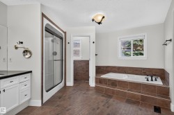 White vanity cabinetry with a black countertop, a framed shower enclosure with sliding glass doors, a built-in bathtub with tiled surround, and tiled flooring - 