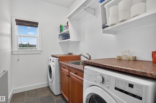 Utility room featuring a window, built-in cabinetry, upper shelving, a utility sink, and tiled flooring - 1251 Summerside Drive Sw, Edmonton, AB 