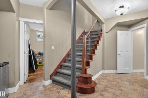 Wood-finish staircase with carpeted treads and decorative iron balusters - 1251 Summerside Drive Sw, Edmonton, AB 