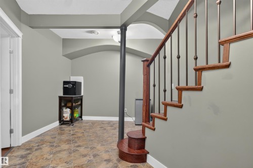 Hardwood staircase with wrought iron balusters, arched wall features, neutral wall color, and patterned floor tile - 1251 Summerside Drive Sw, Edmonton, AB 