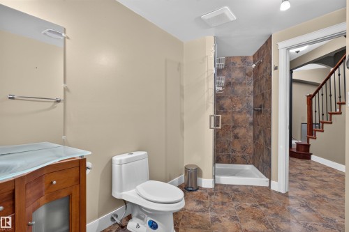 Full bathroom with a tiled walk-in shower, wood-finish vanity with a glass countertop, and patterned floor tiling - 1251 Summerside Drive Sw, Edmonton, AB 